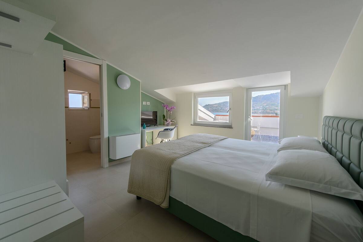 Ein Schlafzimmer mit Bett, Schreibtisch und Blick ins Freie.