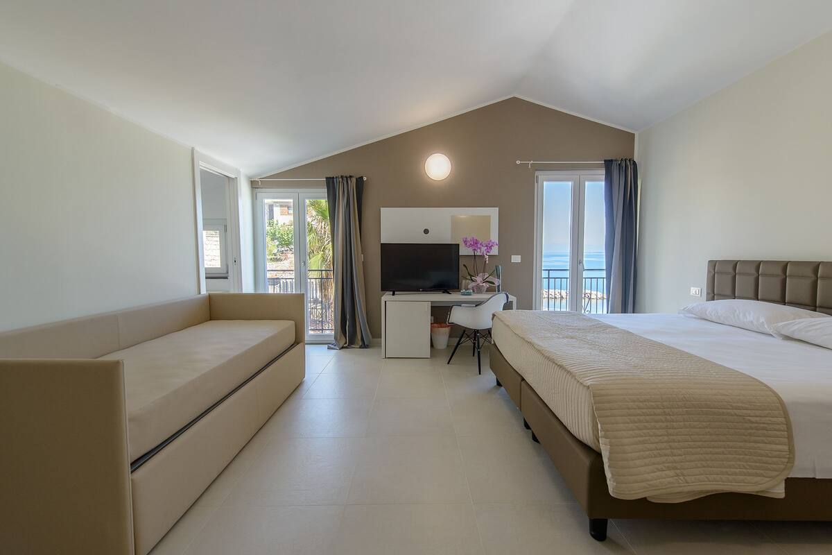 Ein modernes Schlafzimmer mit Bett, Sofa, Schreibtisch und Fernseher.