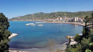 A coastal town with a clear view of the sea, a sandy beach, and a hilly backdrop.
