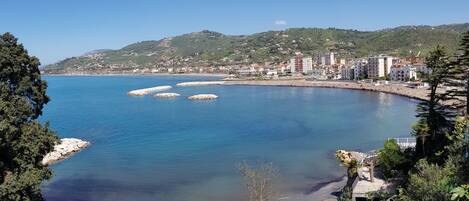 Un pueblo costero con vistas despejadas al mar, una playa arenosa y un paisaje montañoso de fondo.