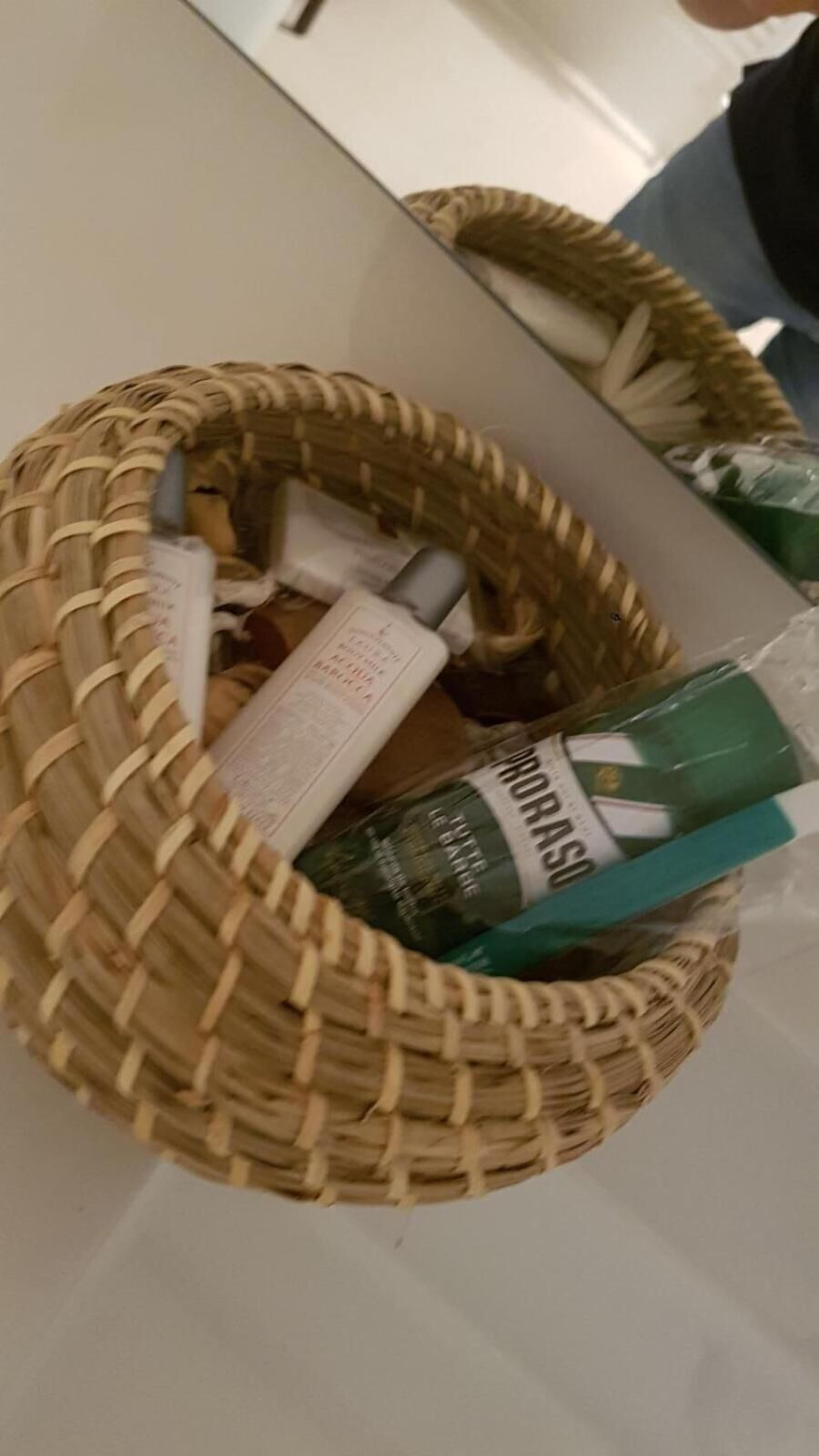 Ein Korbwesen mit Pflegeartikeln und einer grünen Packung, möglicherweise ein Lebensmittel, auf einer weißen Oberfläche.