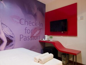 A hotel room with a bed, a red desk, a television mounted on the wall, and a poster with the text "Check-In for Passion". - Check In Hotel (Kuala Lumpur)
