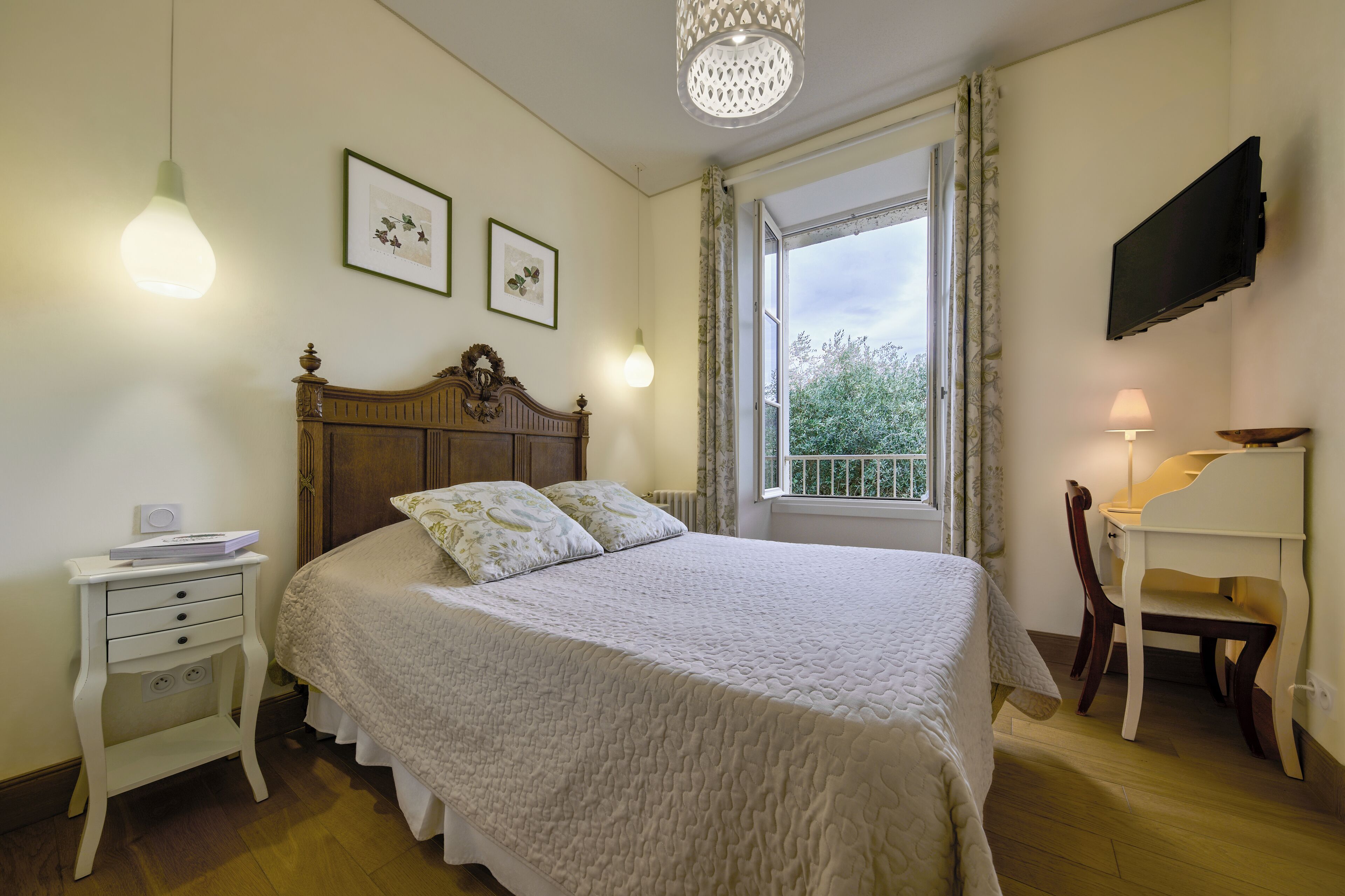 Un dormitorio con cama, mesita de noche, lámpara, silla, televisor y ventana con vistas.