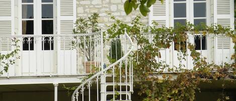 Un bâtiment en pierre avec des volets blancs, un escalier en colimaçon et une végétation luxuriante.