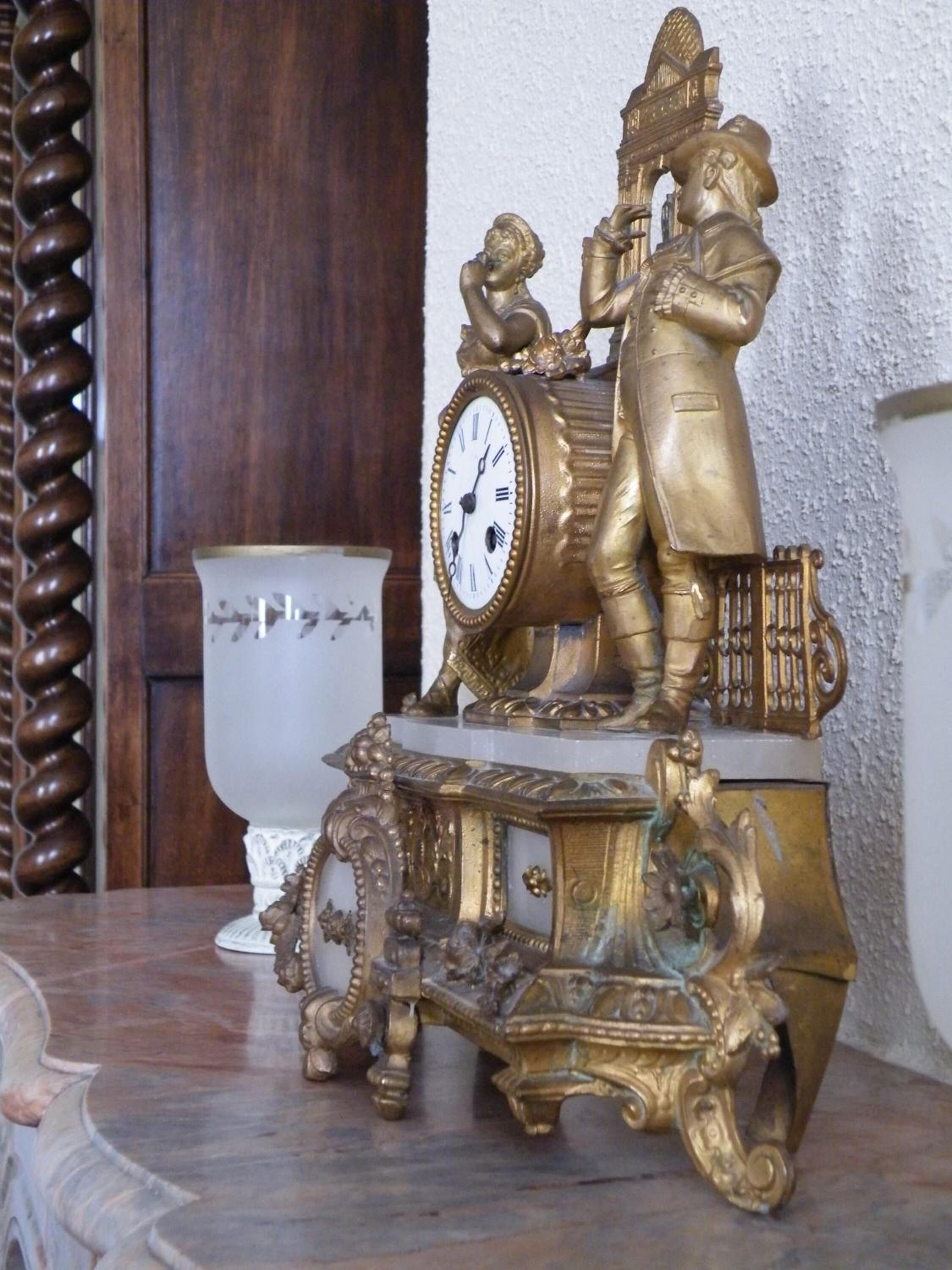 Un reloj decorativo con una figura tocando la batería, sobre un pedestal ornamentado.