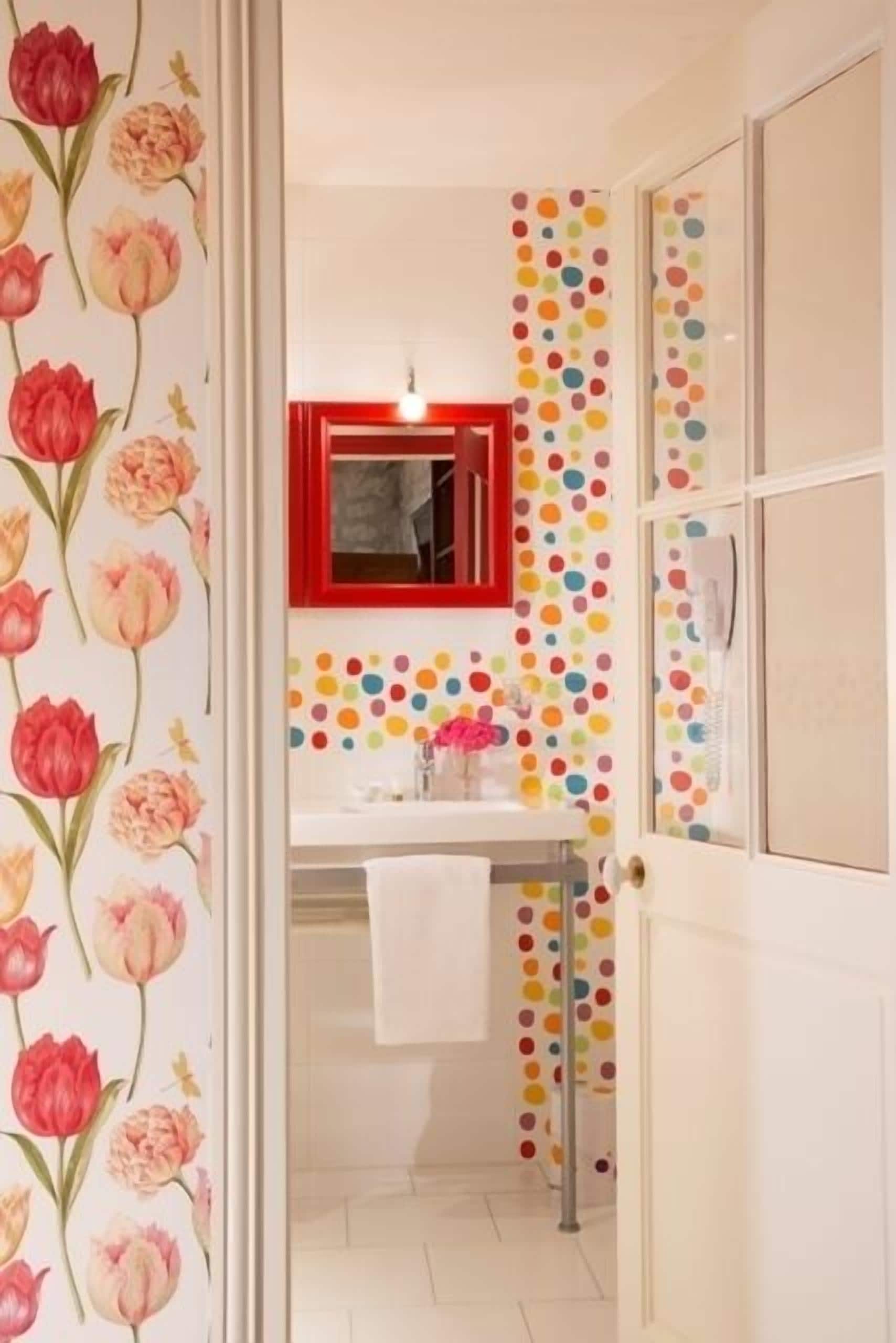 Un baño con papel tapiz floral, un espejo con marco rojo y un diseño de lunares en la pared.