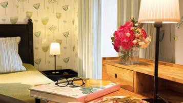 Un dormitorio ordenado con cama, mesita de noche, lámpara y un libro con gafas encima.