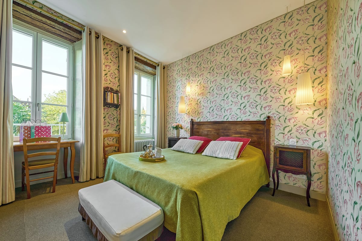 A neatly arranged bedroom with a bed, a bedside table, a chair, and a window with curtains.