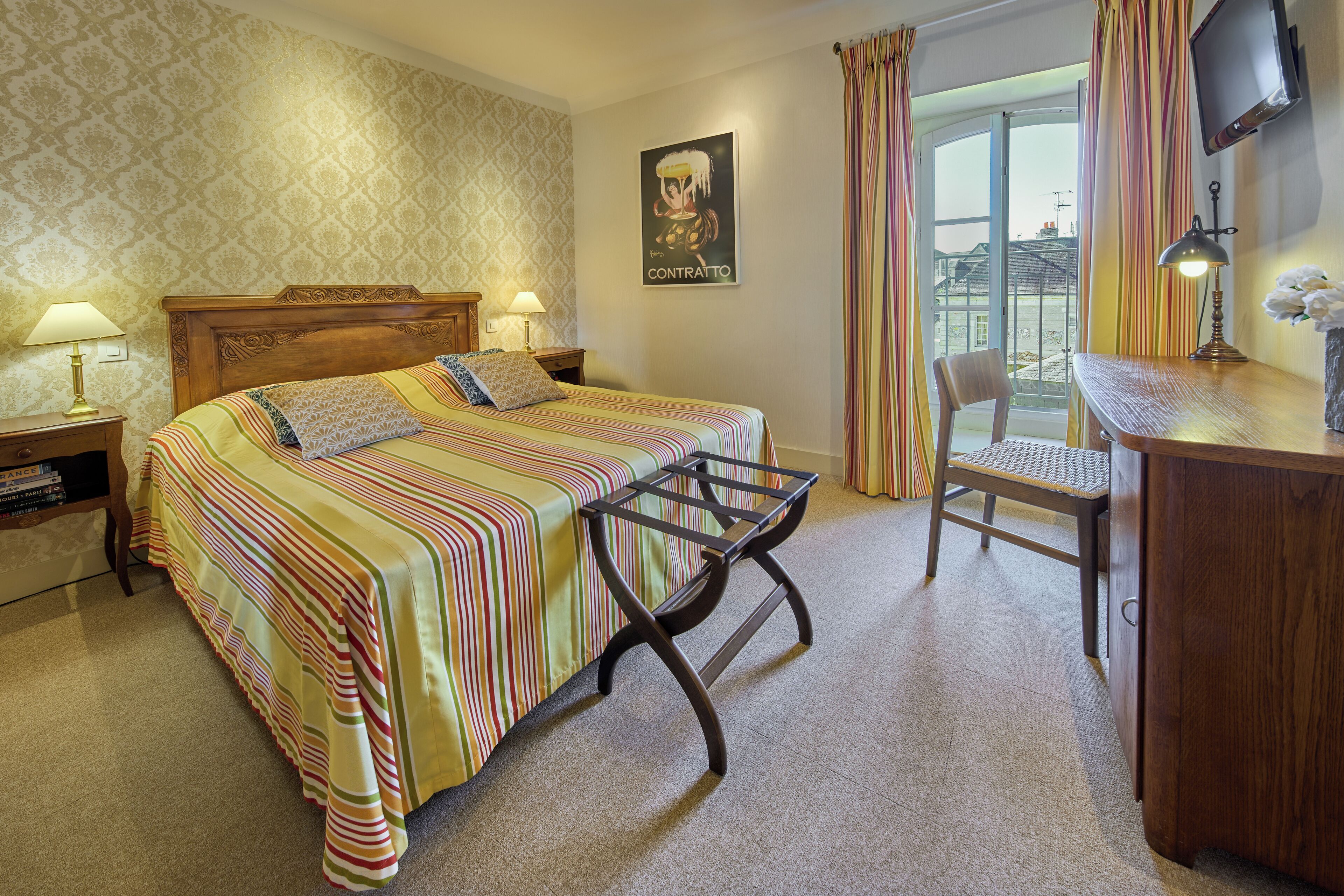 A hotel room with a bed, a desk, a chair, a TV, and a window with curtains.