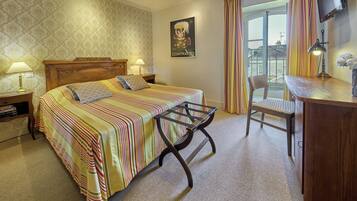 A hotel room with a bed, a desk, a chair, a TV, and a window with curtains.