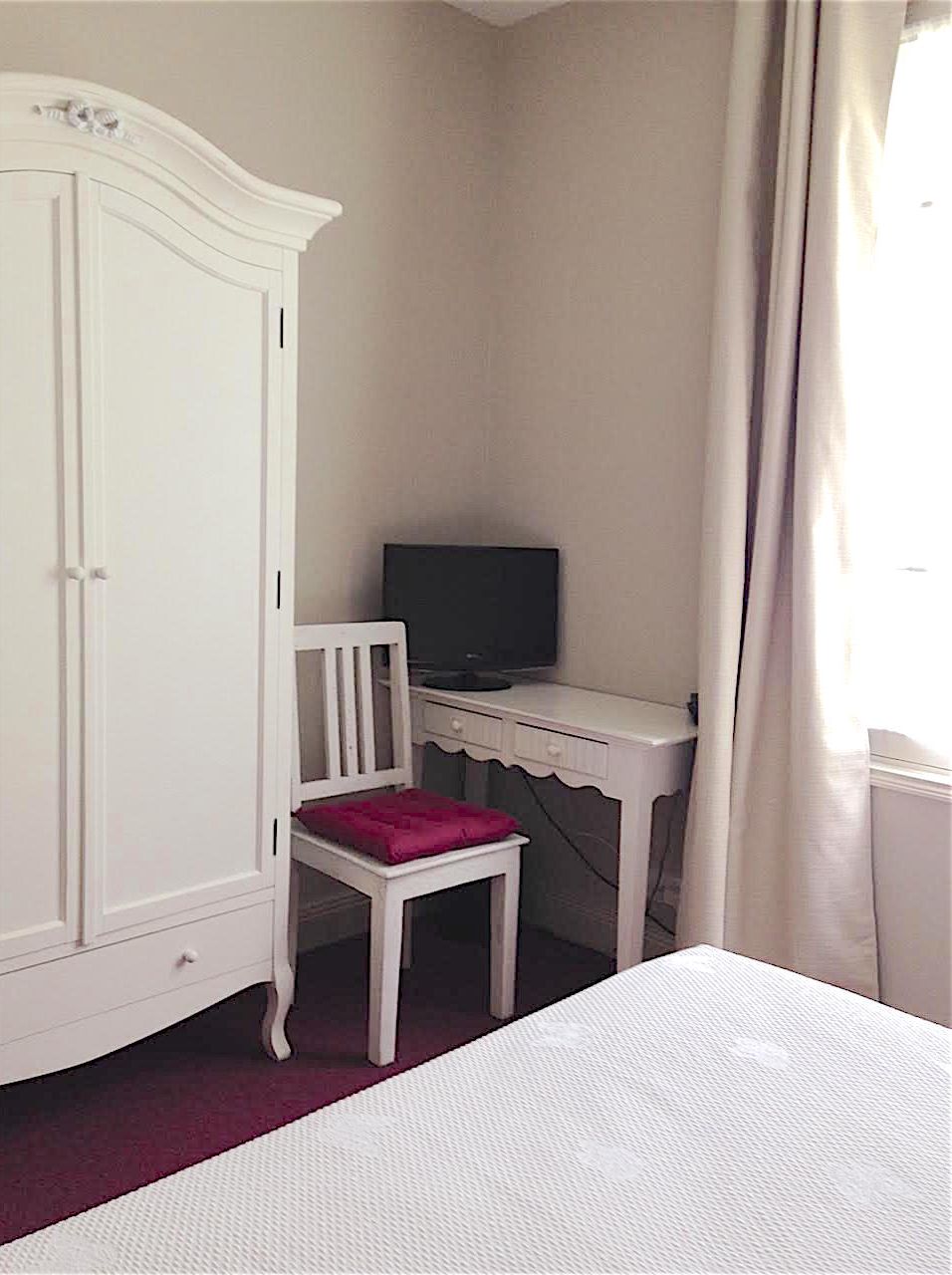 Un dormitorio con una cama, un escritorio con silla, un armario y un televisor.