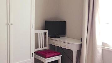 Un dormitorio con una cama, un escritorio con silla, un armario y un televisor.