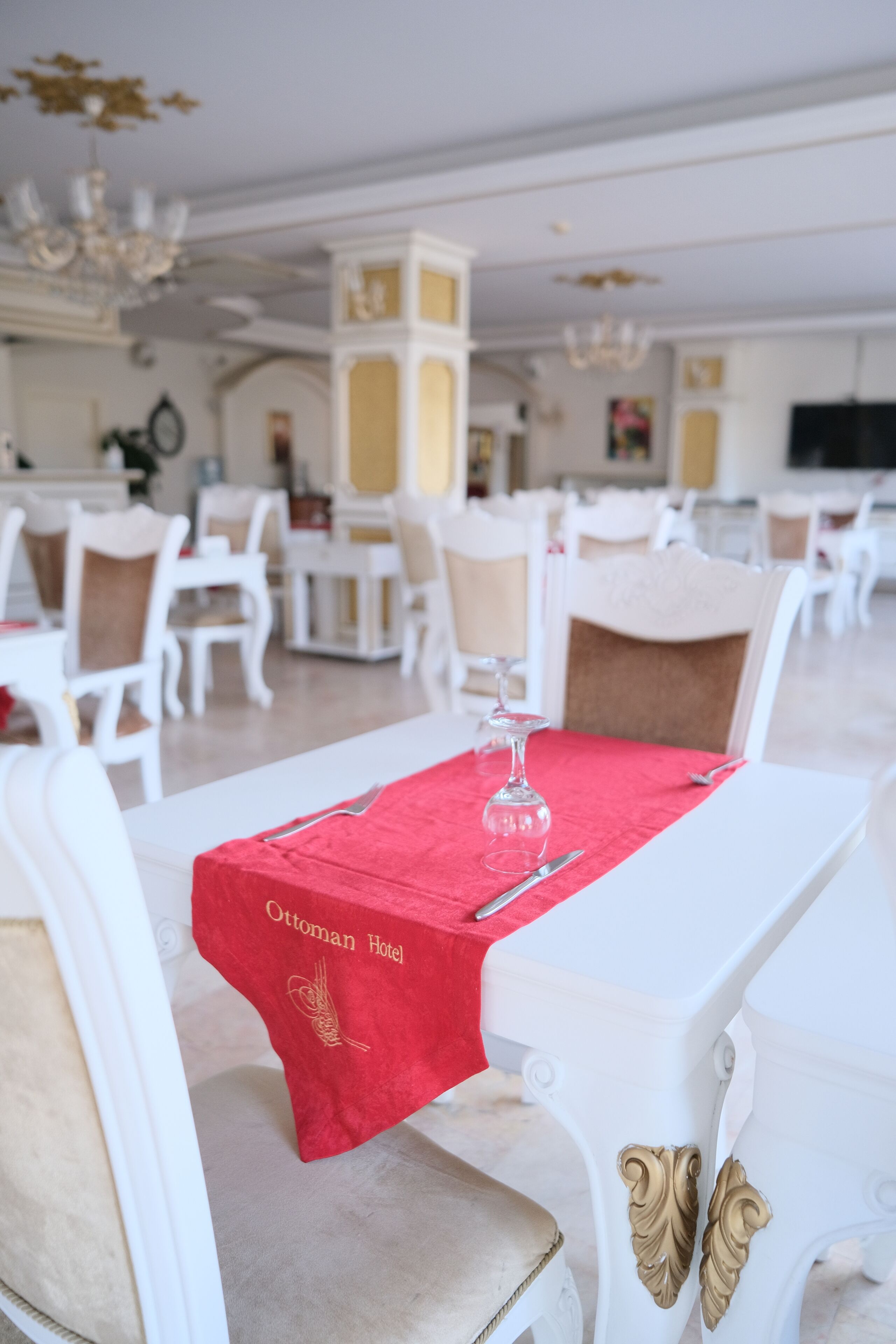 A dining area with white tables and chairs, a red table runner, and a glass on one table.