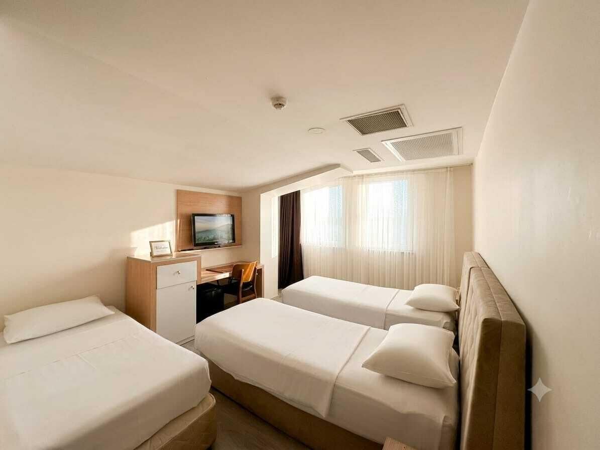 Una camera d'albergo con due letti, una scrivania, una televisione e una finestra con tende.