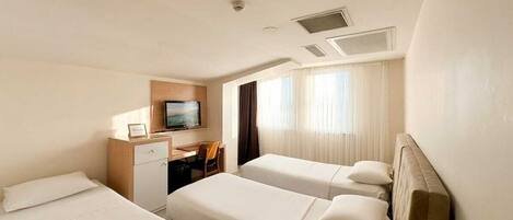 Habitación de hotel con dos camas, un escritorio, un televisor y una ventana con cortinas.