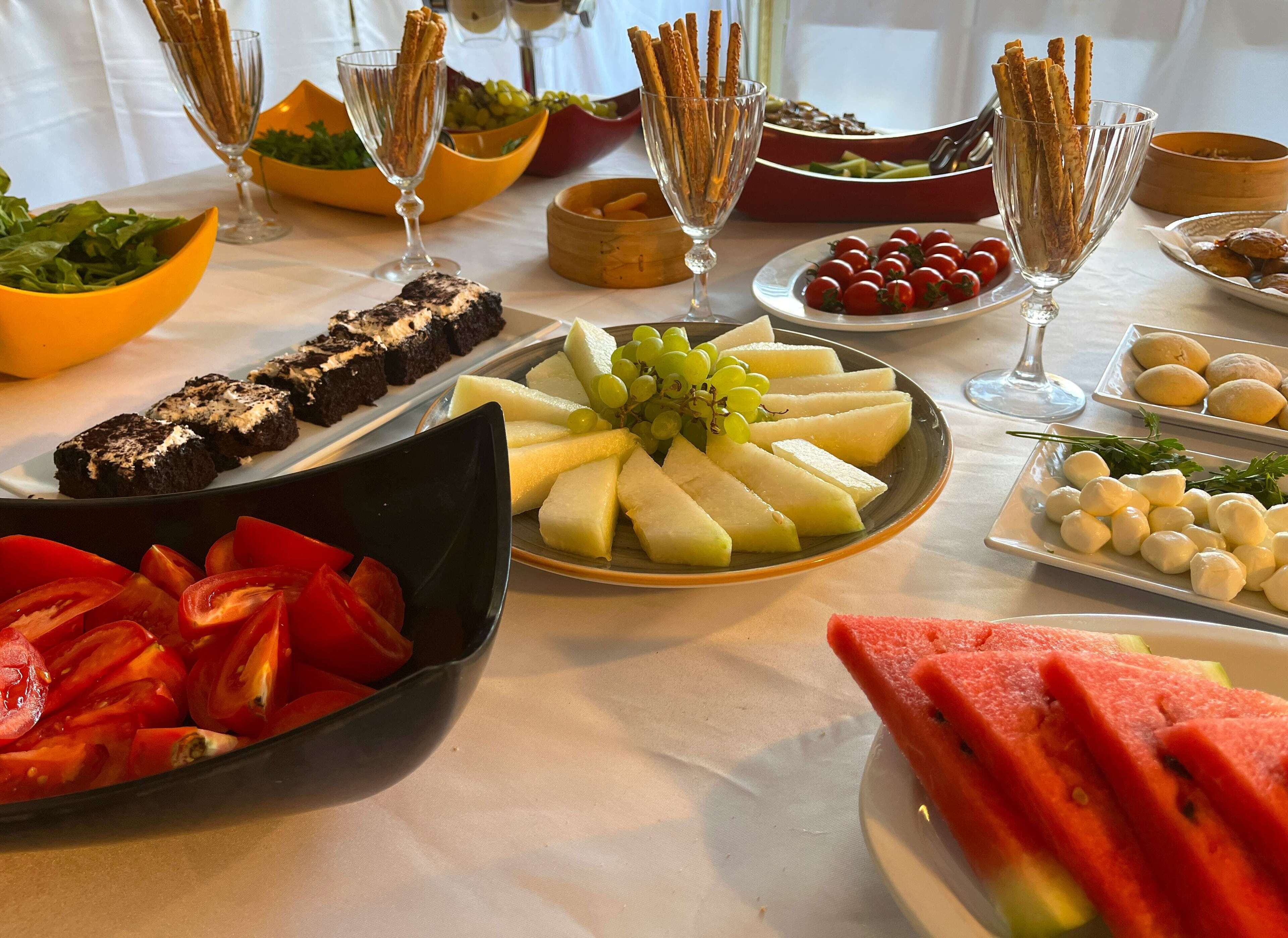 Et bord med forskelligt mad, herunder druer, melon, tomater og grissini.