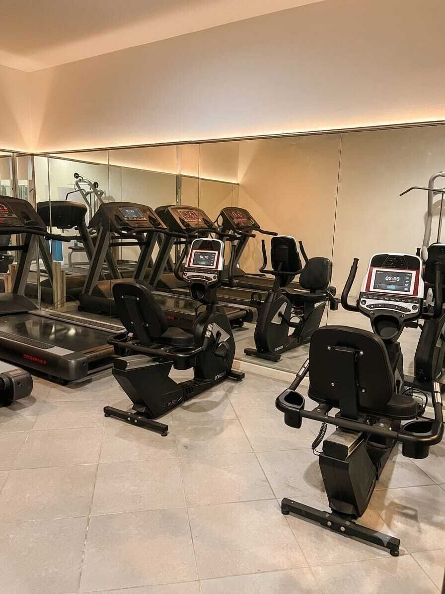 A gym with multiple exercise machines, including treadmills and stationary bikes, arranged in rows.