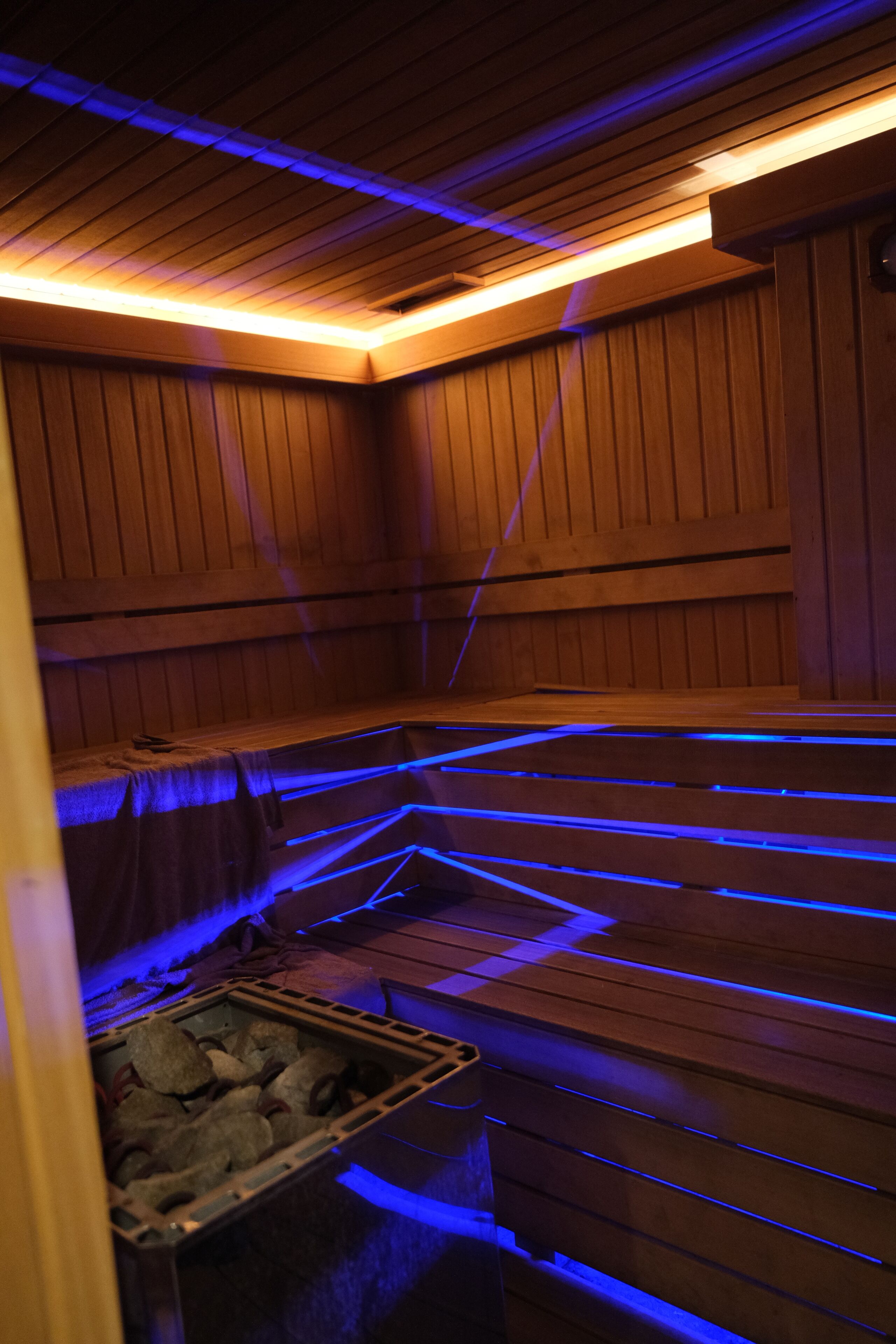 A sauna with wooden walls and benches, and a container of rocks at the bottom.