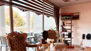 A room with two ornate chairs, a small table, a bookshelf, and a large window with blinds. - Ottoman Hotel Sakarya (Adapazari)