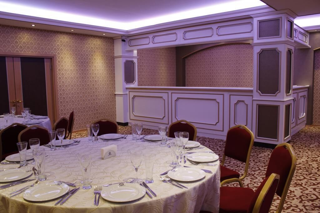 Un salón de banquetes con mesas redondas dispuestas para comer, provisto de platos, cubiertos y vasos.