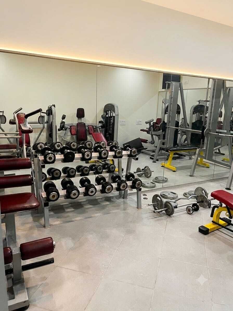 Une salle de sport équipée de divers appareils d’exercice, notamment des haltères, des bancs et des machines de musculation.
