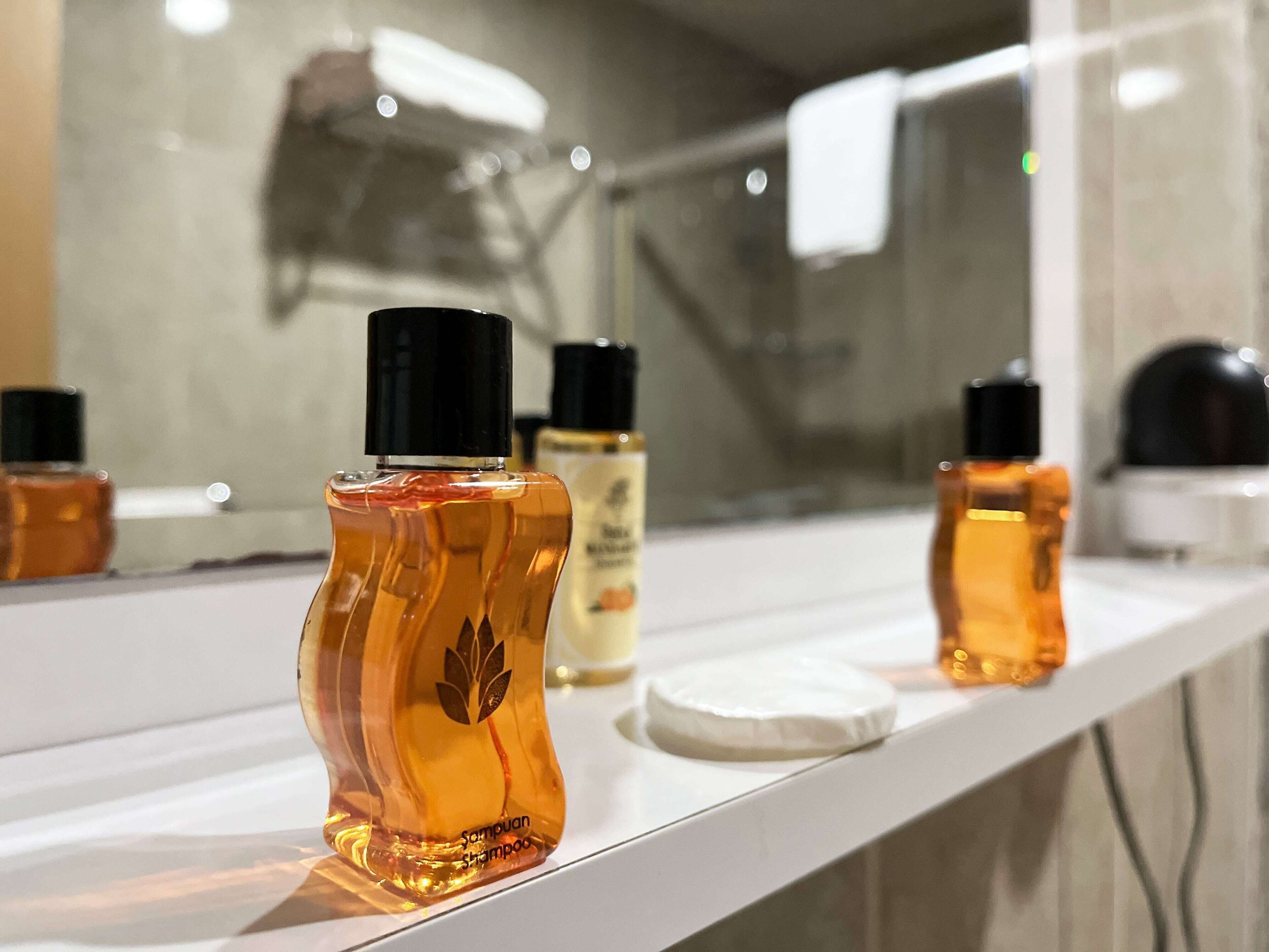 A bathroom counter with a mirror reflecting various toiletries, including a bottle of shampoo.