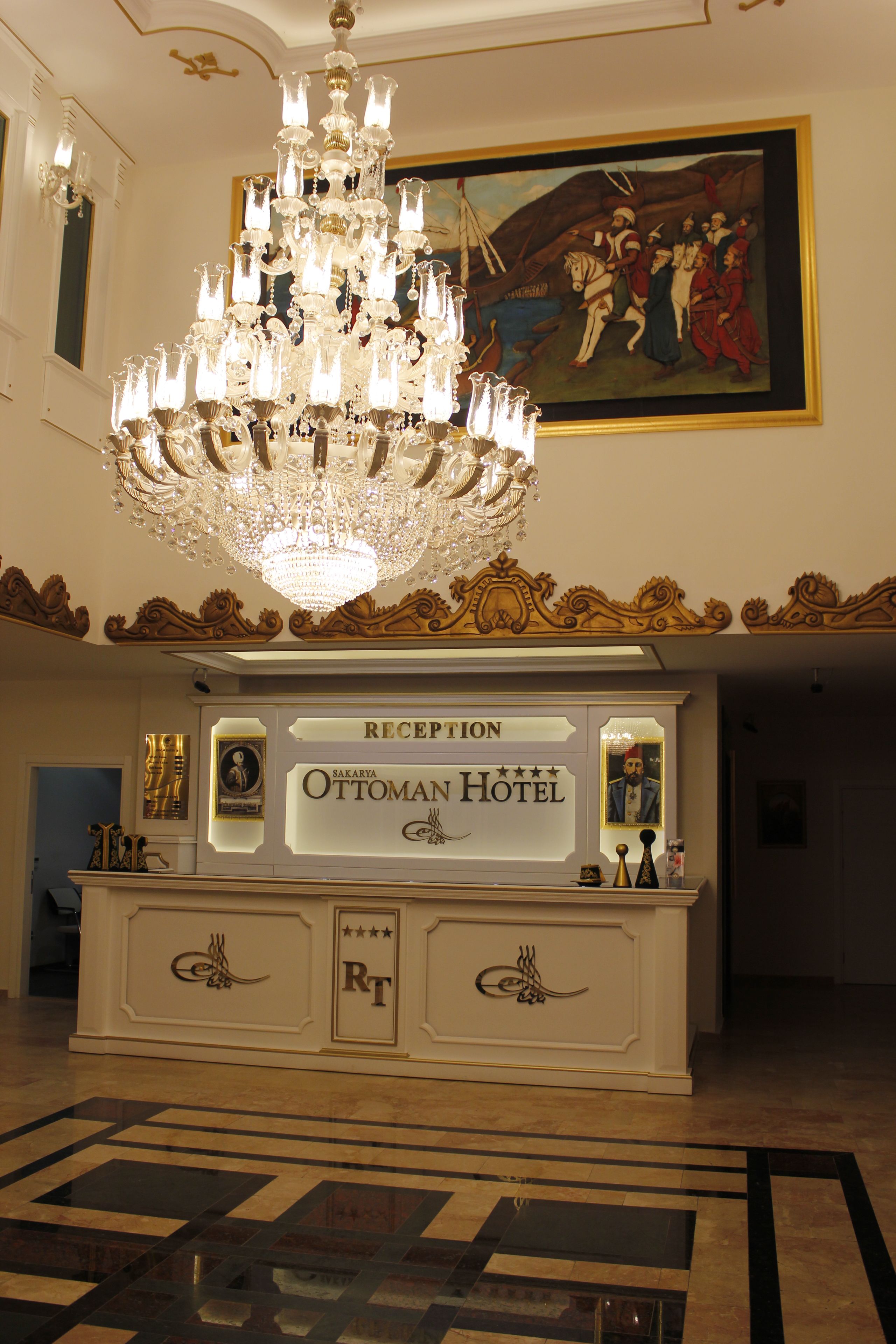 Un área de recepción con una araña, un cuadro y un cartel del Hotel Ottoman.