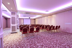 A conference room with rows of red chairs, a projector screen, and patterned carpet. - Ottoman Hotel Sakarya (Adapazari)