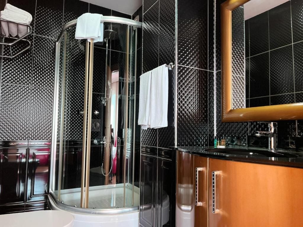 A modern bathroom with a glass-enclosed shower, a white towel, and a black tiled wall.