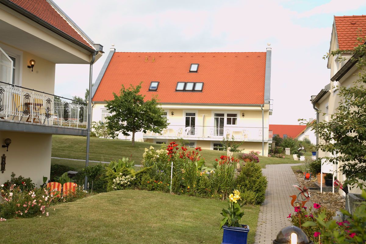 A residential building with a red-tiled roof, a balcony, and a garden with various plants and flowers.