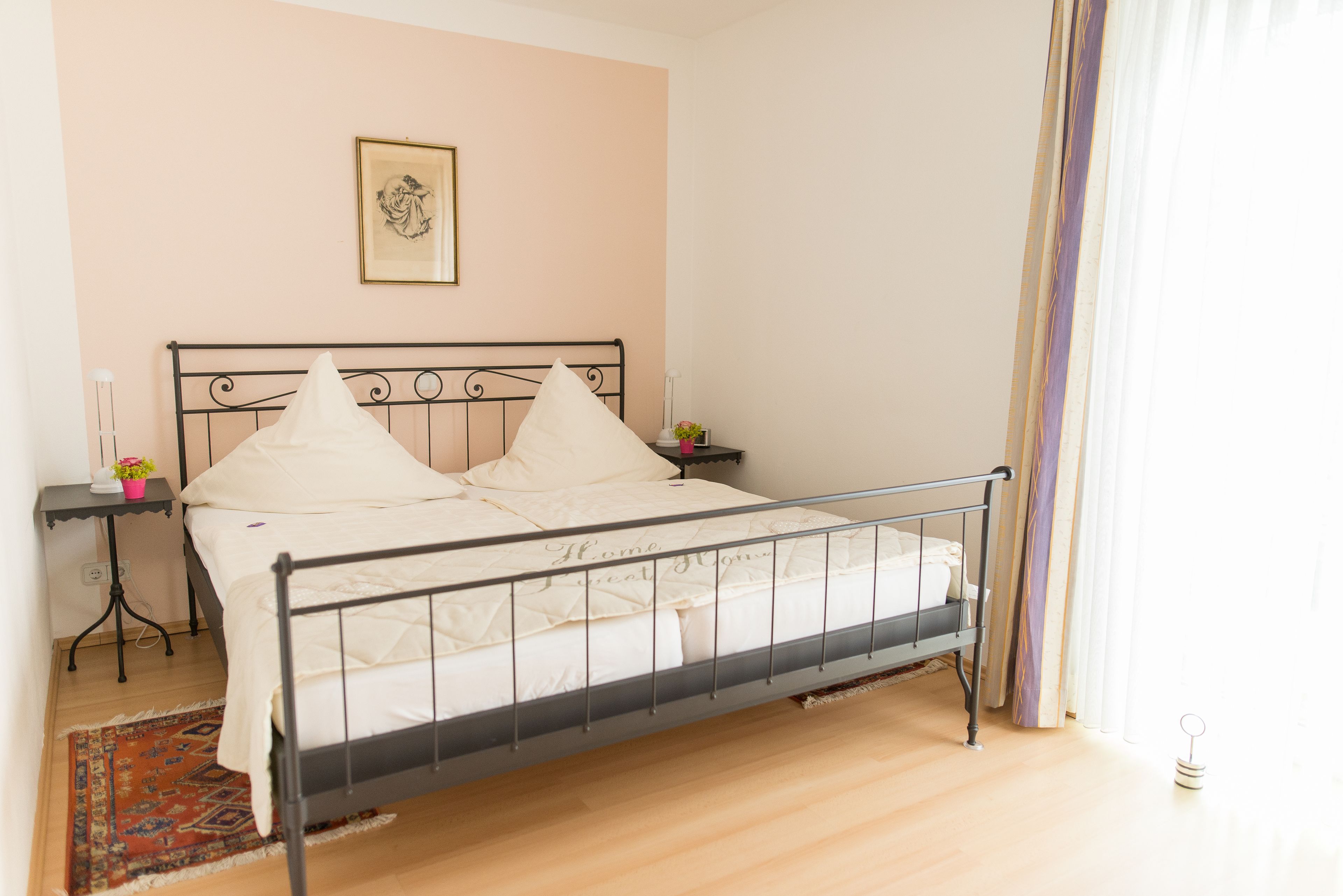 A neatly made bed with a metal frame, a bedside table with a lamp, and a framed picture on the wall.