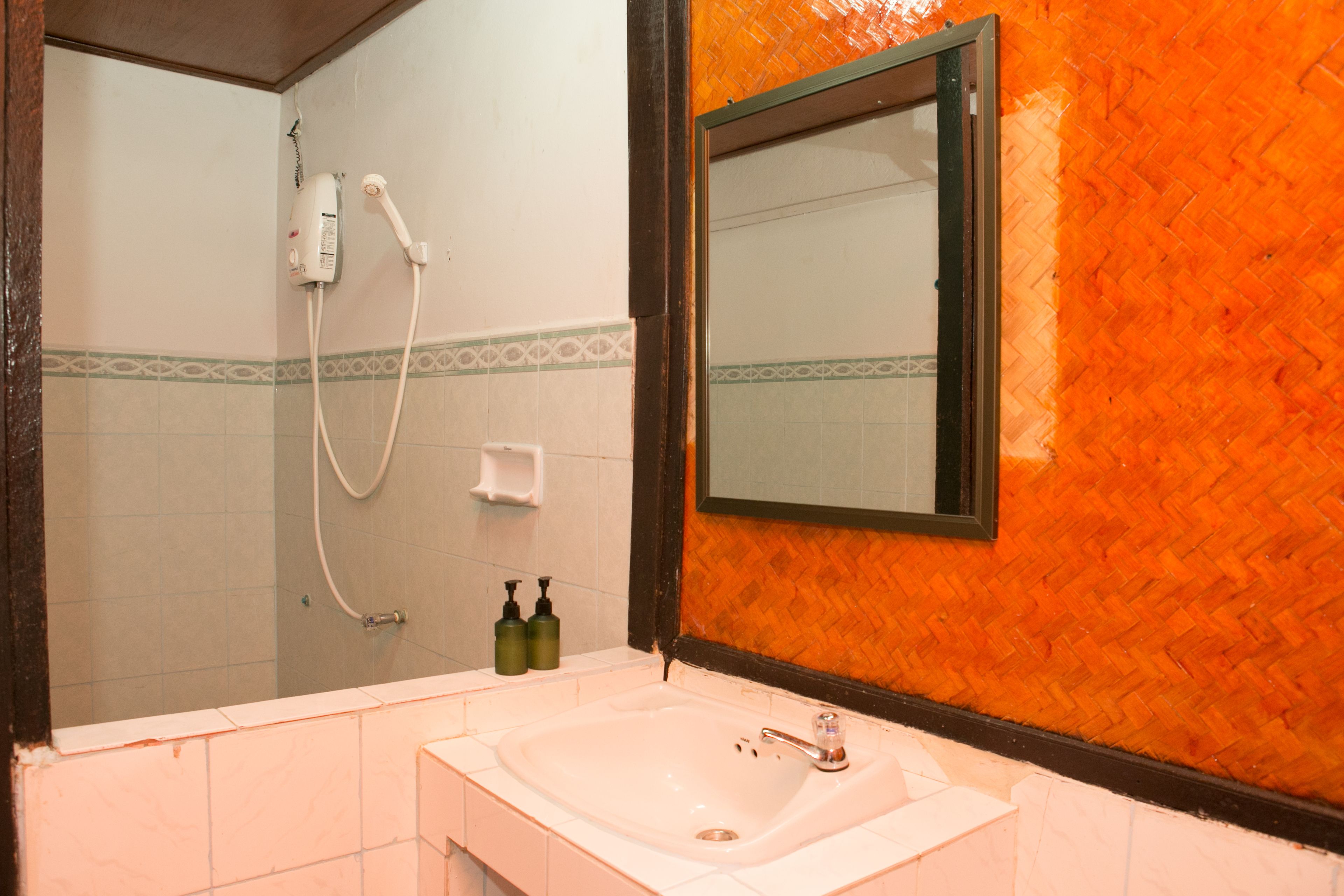 A bathroom with a white sink, a shower, and a mirror with an orange wall.