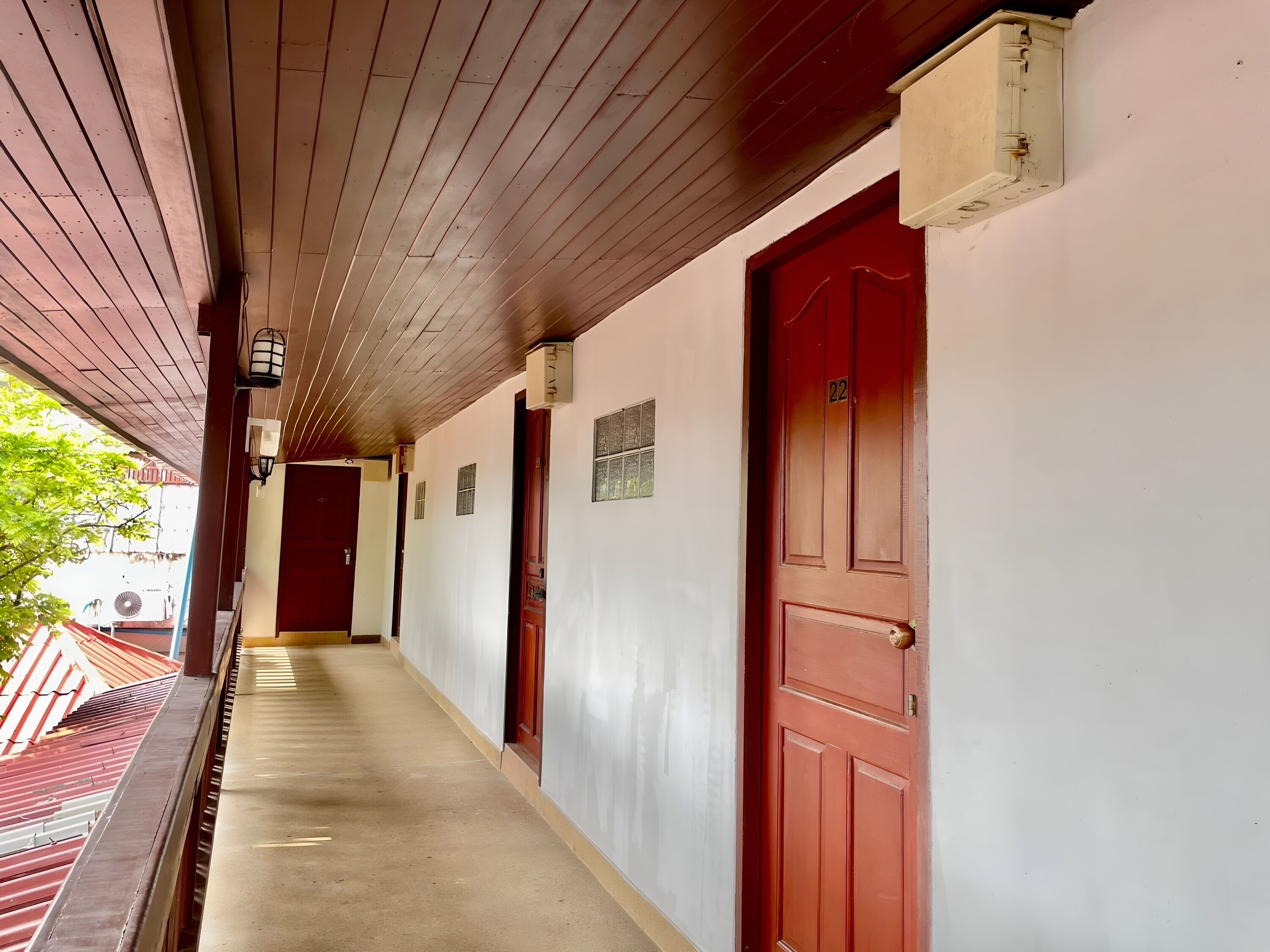 Corredor com teto de madeira e portas vermelhas, que dá acesso a quartos individuais.