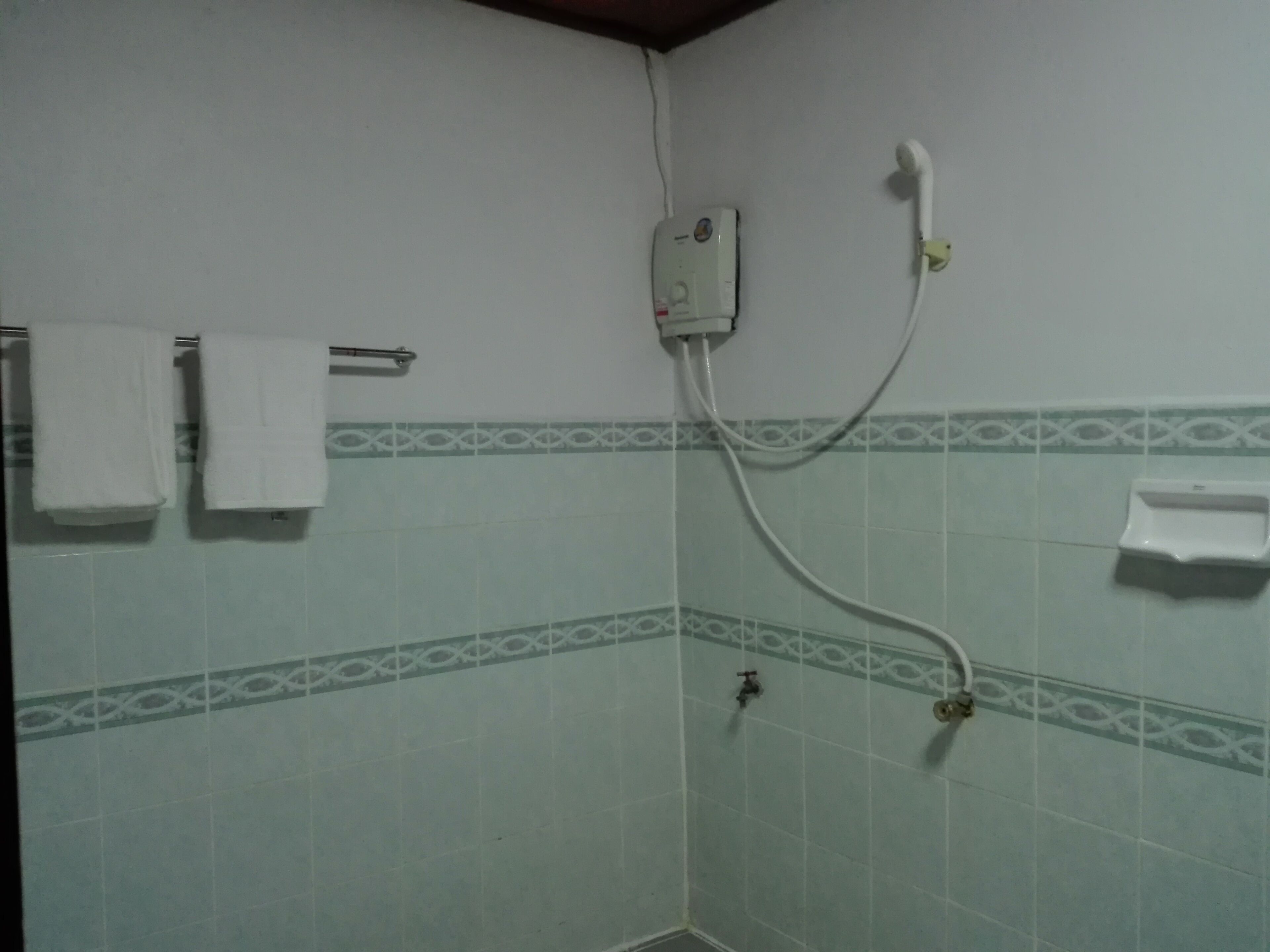A bathroom with a shower, a towel rack with two towels, a soap dispenser, and a patterned tile design on the walls.