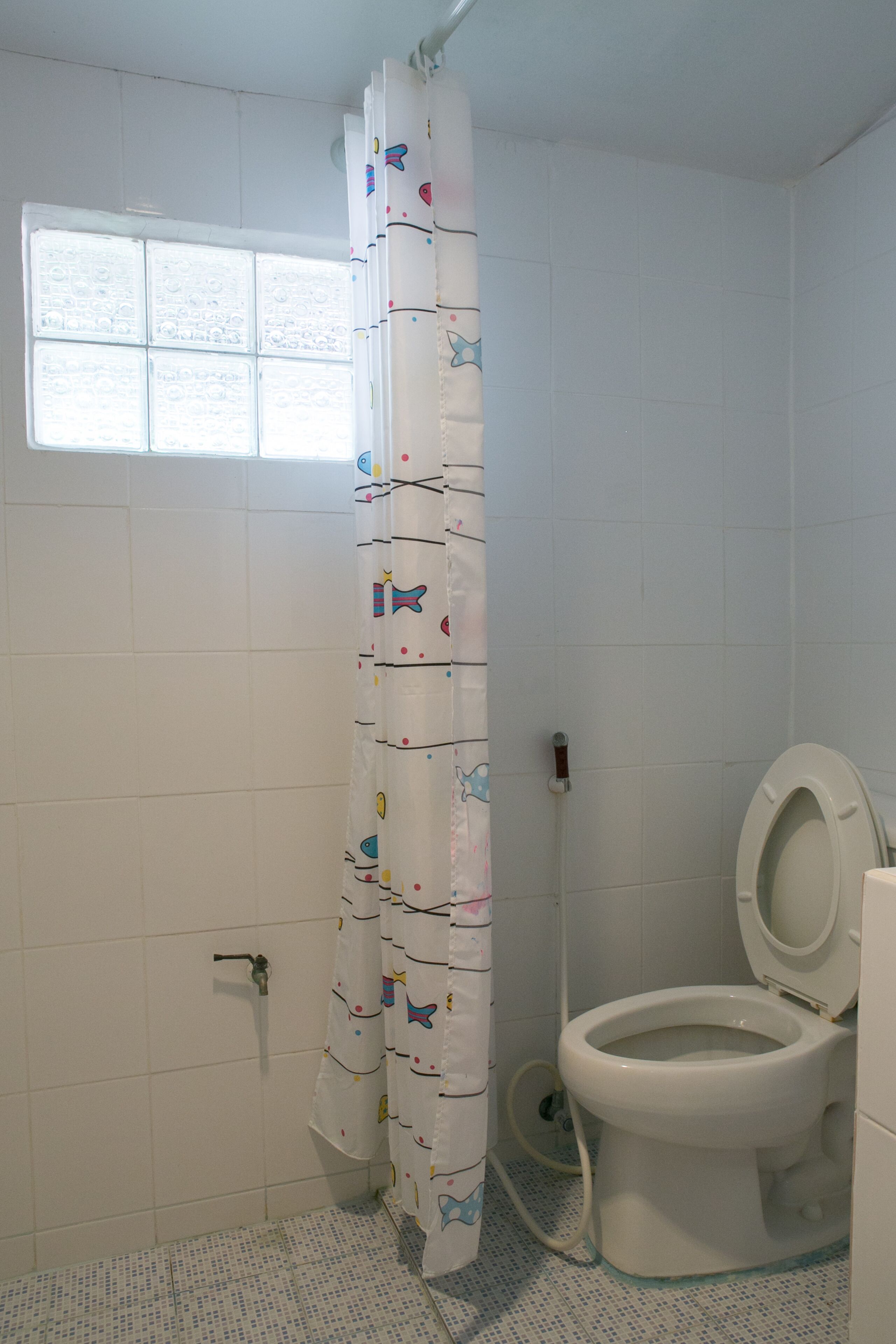 A bathroom with a toilet, a window, and a shower curtain with a pattern.