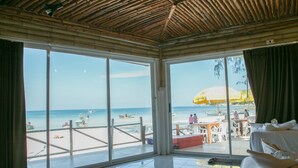 A room with large windows overlooking a beach, a bed, and a view of the beach with umbrellas and people. - Haadrin Resort (Ko Pha-ngan)