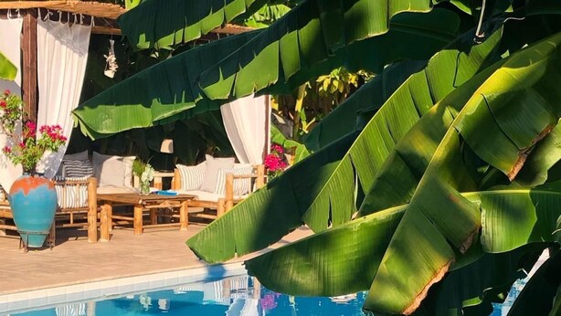 Zona de piscina con terraza de madera, sillas de descanso y un área de estar cubierta con vista a la piscina.