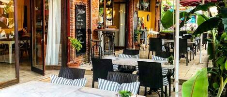 Un café al aire libre con paredes de ladrillo, mesas en la terraza y un panel con la carta.