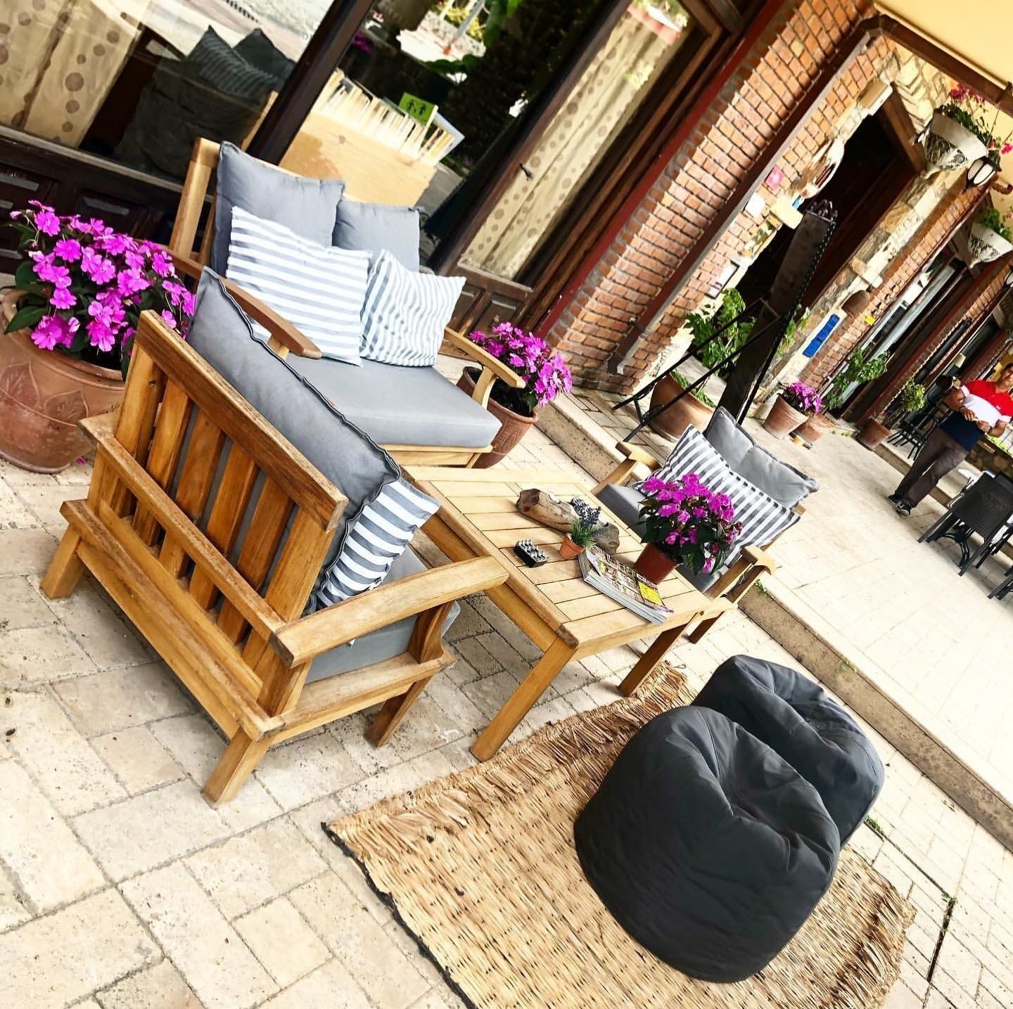 A wooden outdoor seating area with a sofa, chairs, and a table, surrounded by potted plants and flowers.