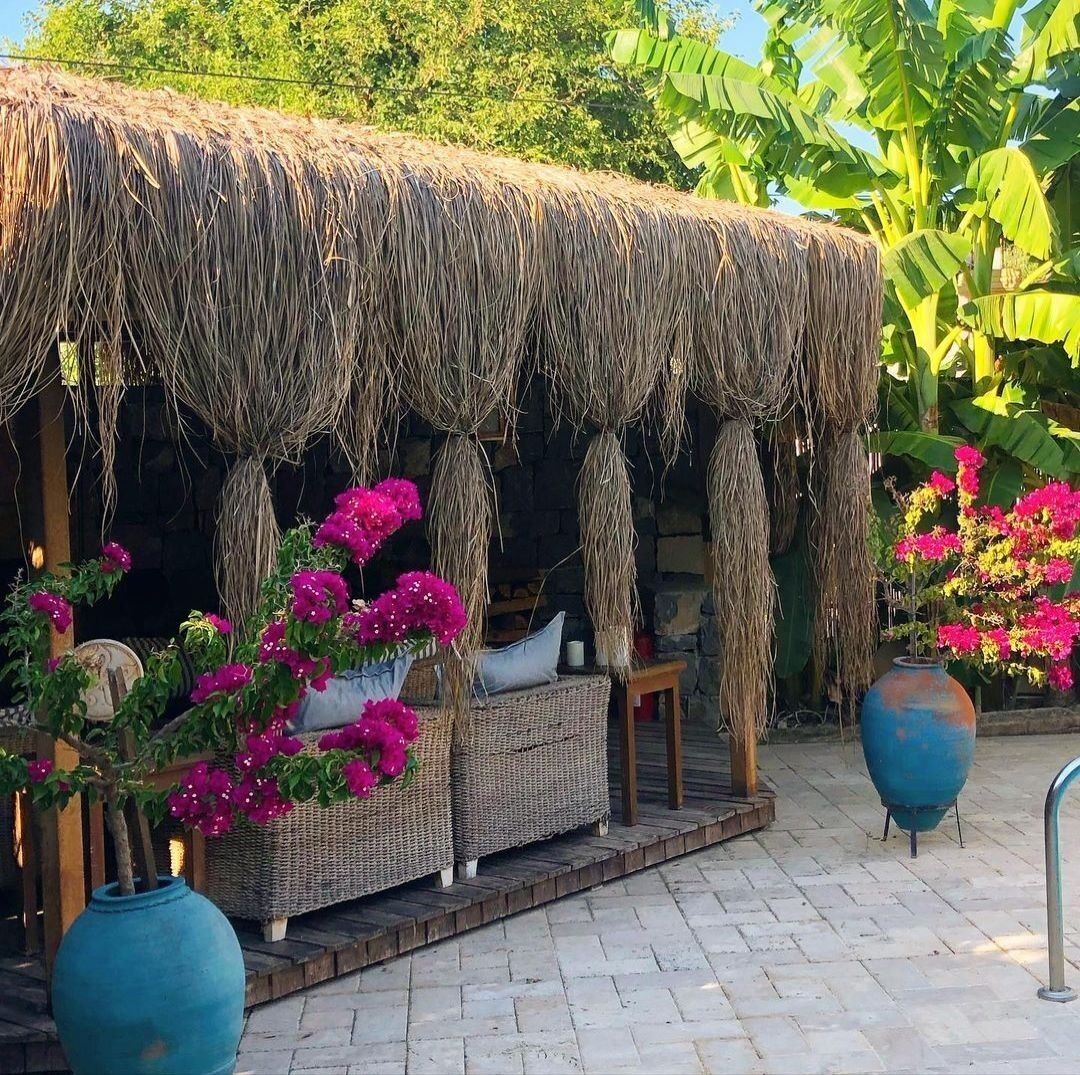 A thatched-roof outdoor seating area with wicker furniture and potted bougainvillea plants.