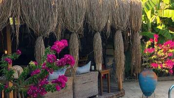 A thatched-roof outdoor seating area with wicker furniture and potted bougainvillea plants.