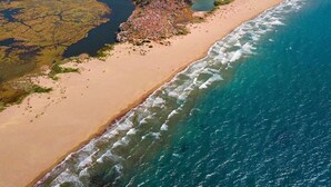 Vista aérea de una zona costera con playa, aguas cristalinas y colinas circundantes.