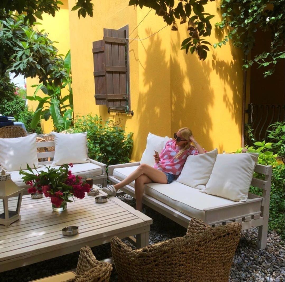 Eine Person sitzt auf einem weißen Outdoor-Sofa mit Kissen, einem Tisch mit Blumen in einer Vase und Korbwannen.