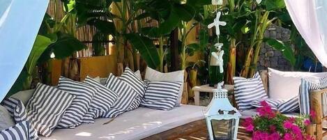 Un espace de détente extérieur accueillant, avec un banc rembourré, des coussins à rayures et une table en bois.