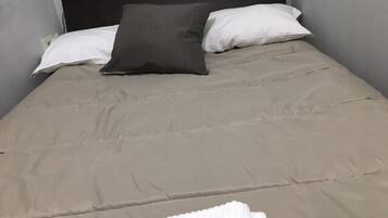 A single bed with a grey headboard, a beige bedspread, and two pillows (one white, one dark grey).