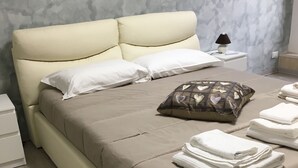 A neatly made bed with white and patterned pillows, a folded white towel, and a lamp on a bedside table. - Almayer La Locanda della Bicicletta (Gaeta)