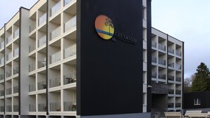 Un hôtel à plusieurs étages, doté d’un design moderne, avec des balcons et un logo représentant un arbre et un soleil.