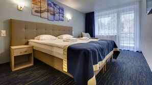 Une chambre d’hôtel avec un grand lit, une table de chevet, une commode, une fenêtre avec des rideaux et des œuvres d’art accrochées au mur.