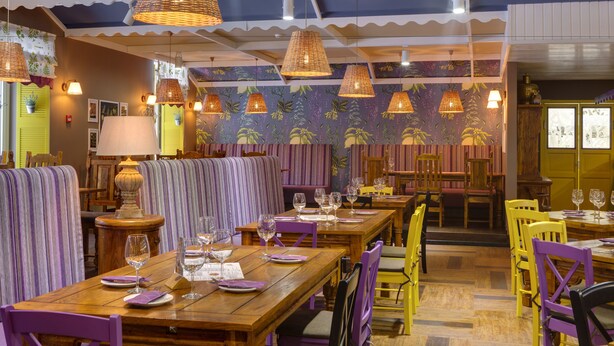 Un restaurant avec des banquettes et des tables à rayures, des meubles en bois et des lampes en osier suspendues au plafond.
