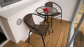 Un petit balcon avec deux fauteuils en osier et une table en verre, agrémenté de deux pommes rouges.